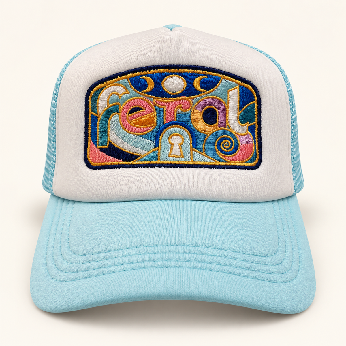 Front view of a white and aqua mesh trucker hat with colorful lowercase FERAL embroidery, moons, a keyhole and gold outlines.