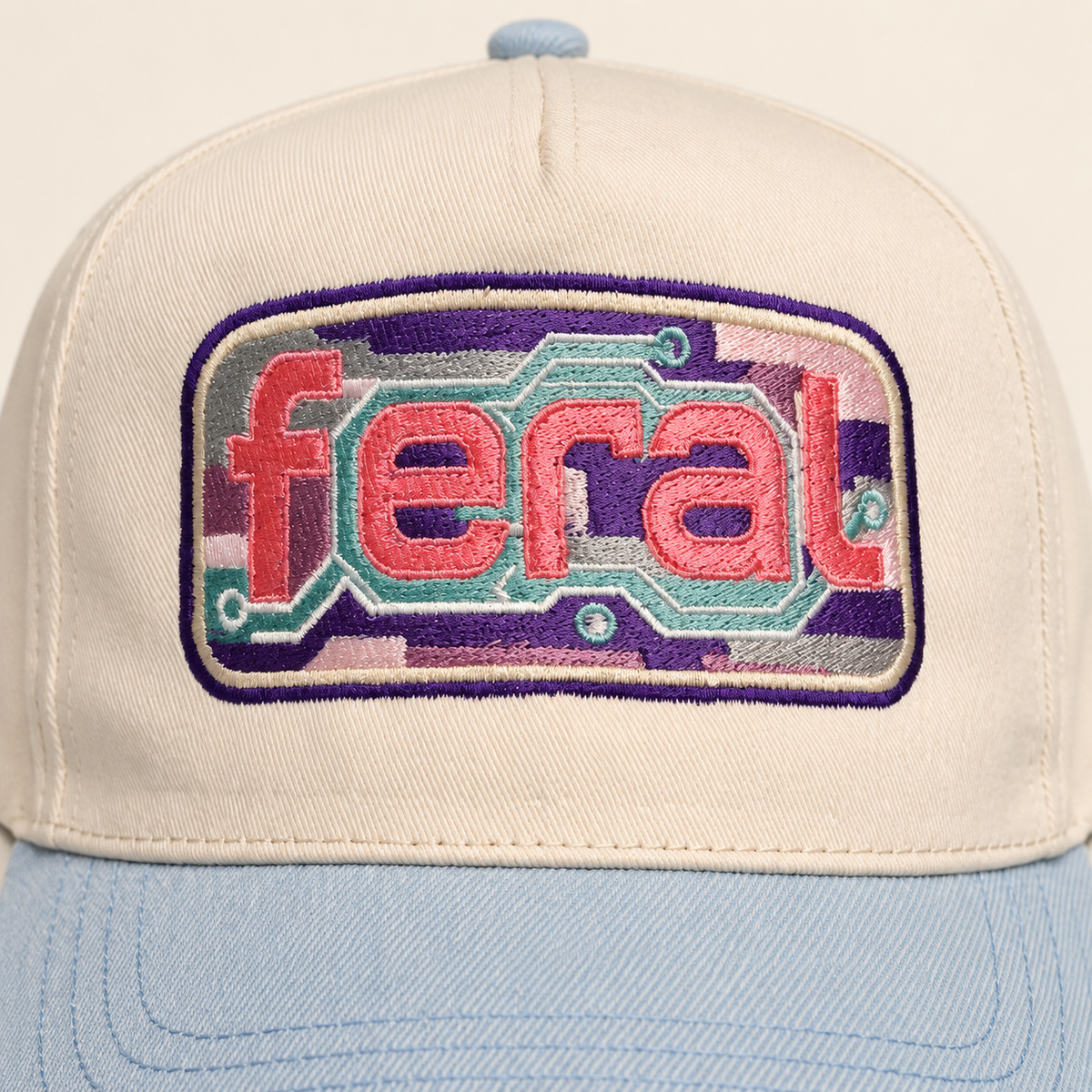 Close-up of the colorful cassette-inspired FERAL embroidery on the cream and powder-blue hat.