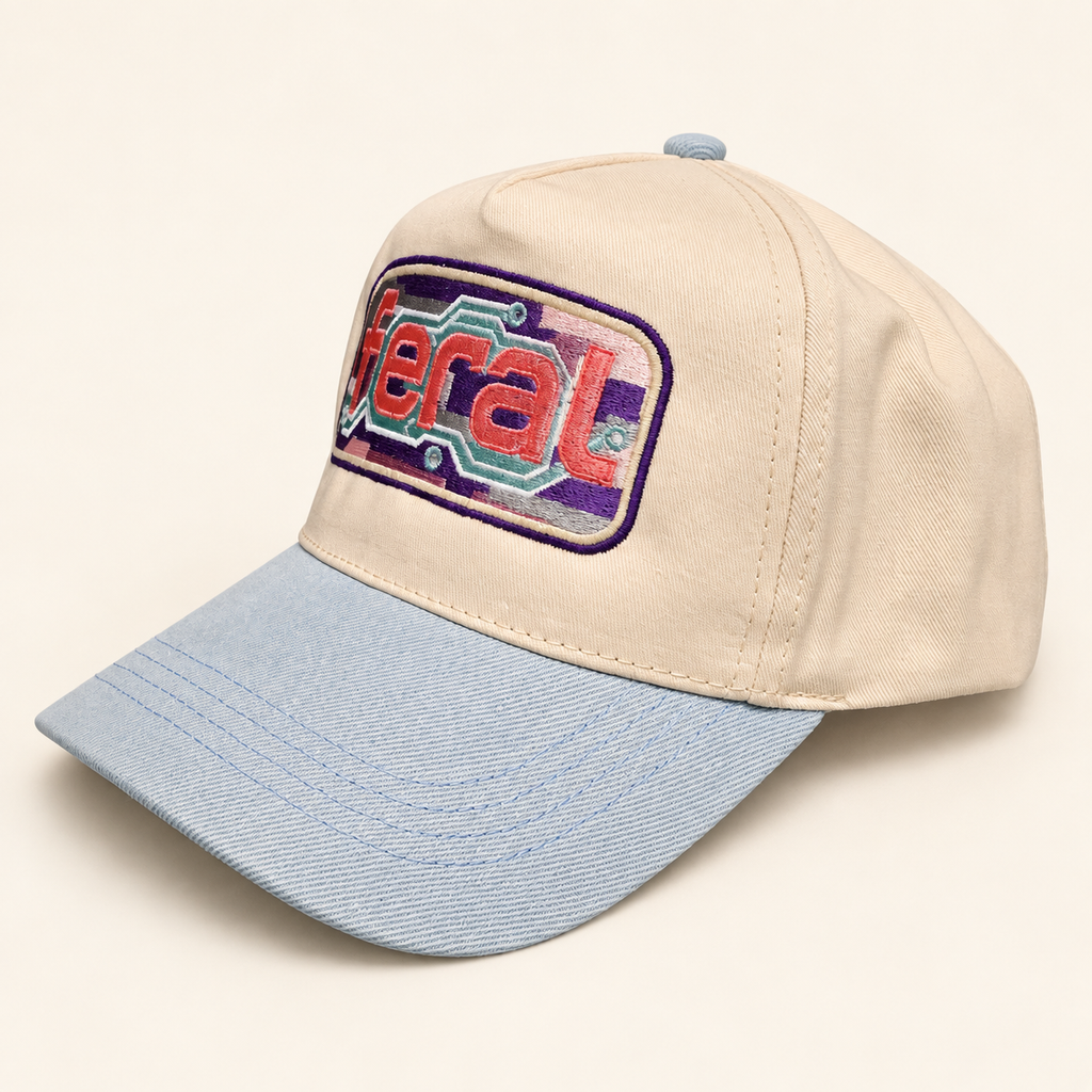 Three-quarter view of the cream FERAL cassette embroidered hat with a powder-blue brim and solid fabric panels.