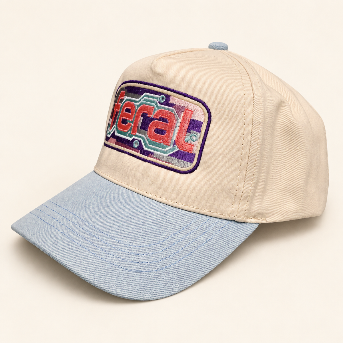Three-quarter view of the cream FERAL cassette embroidered hat with a powder-blue brim and solid fabric panels.