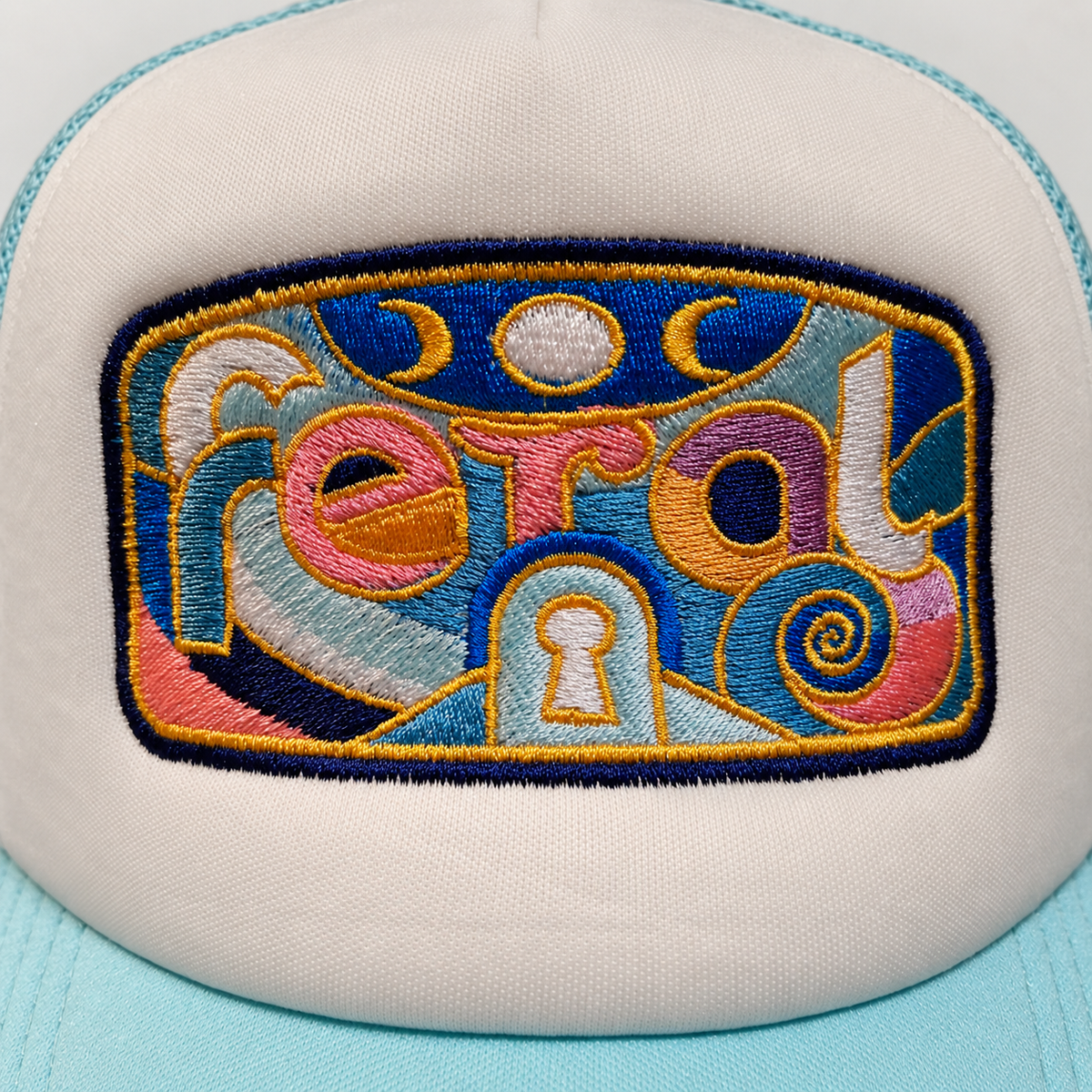 Close-up of colorful FERAL embroidery on a cream and pale aqua trucker hat.