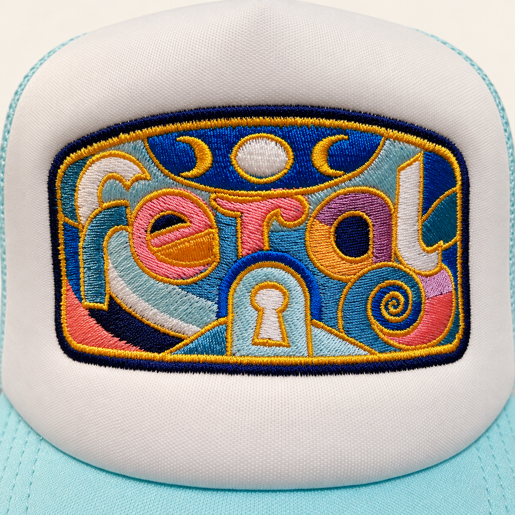 Close-up of the multicolor lowercase FERAL embroidery with moons, a spiral, central keyhole, gold outlines and navy border.