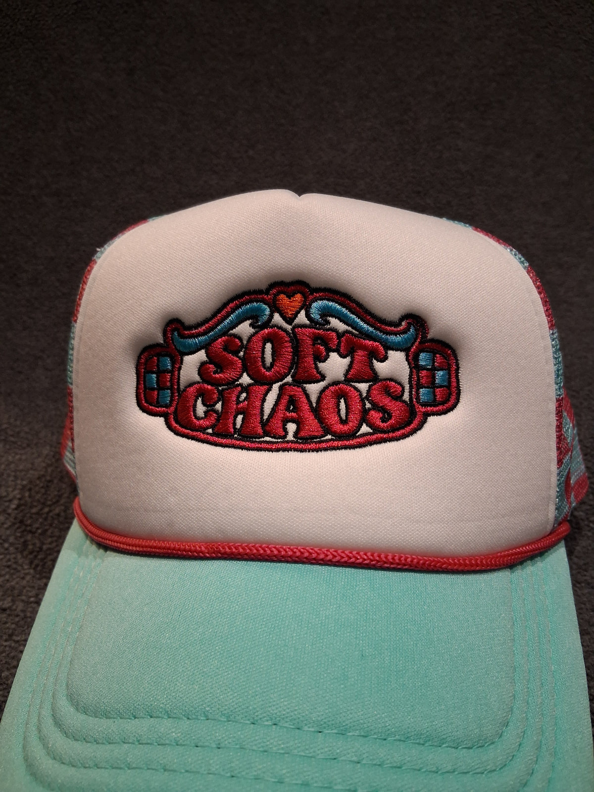 Close-up of the Soft Chaos machine embroidery with pink lettering, teal scrollwork, checker accents, dark outlines and an orange heart.