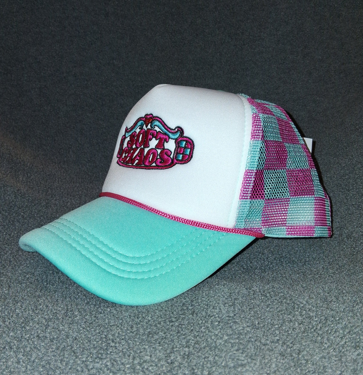 Opposite side of the Soft Chaos embroidered trucker hat, showing the pink-and-teal gingham mesh and teal bill.
