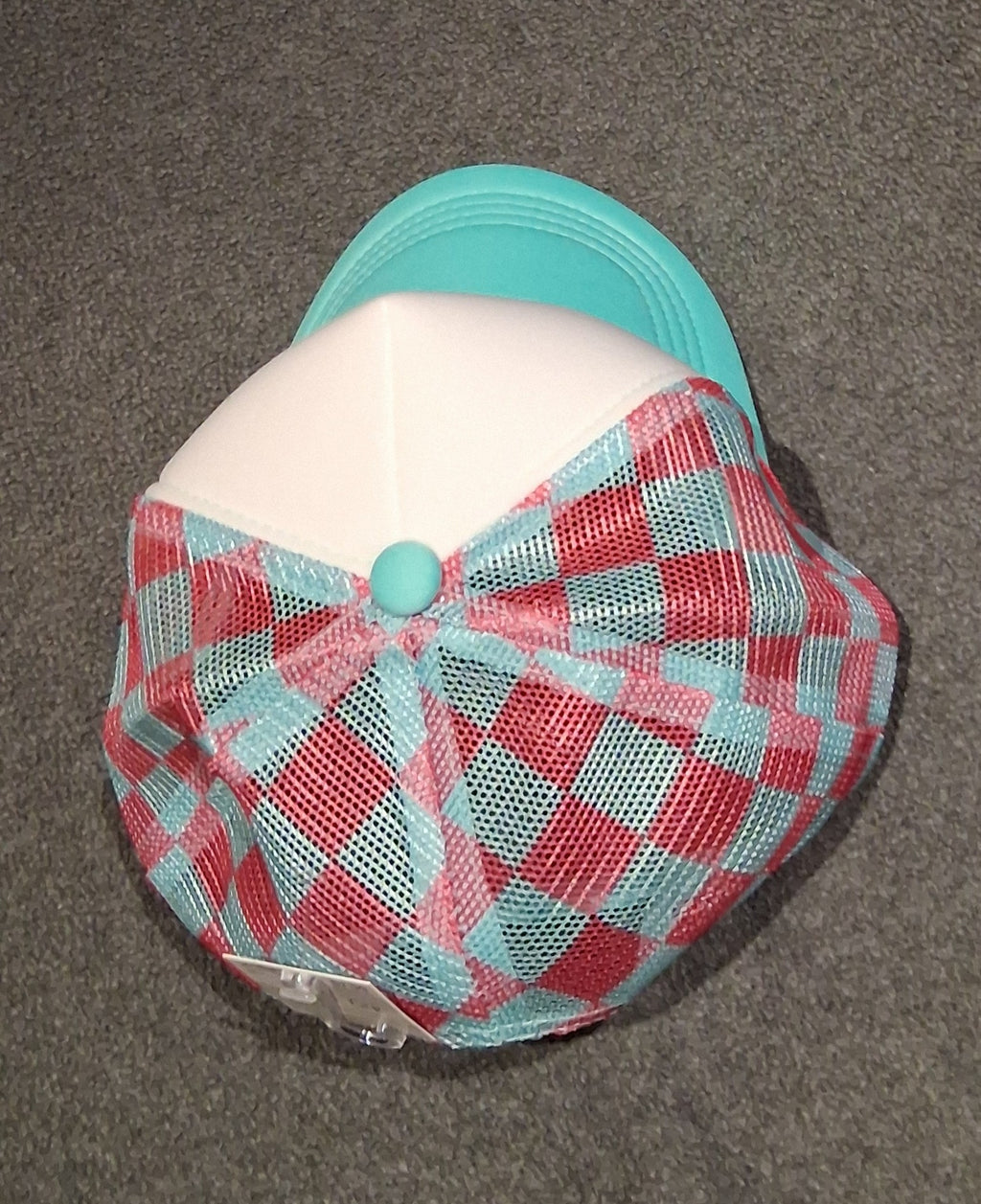 Top view of the Soft Chaos trucker hat showing its teal button, white front panel and pink-and-teal gingham mesh crown.